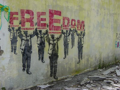 photo of a wall painted with the word "freedom" where each letter of the word is held up by a human figure and represents a particular type of freedom